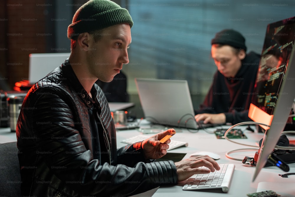 Criminal with plastic card looking at computer screen in office