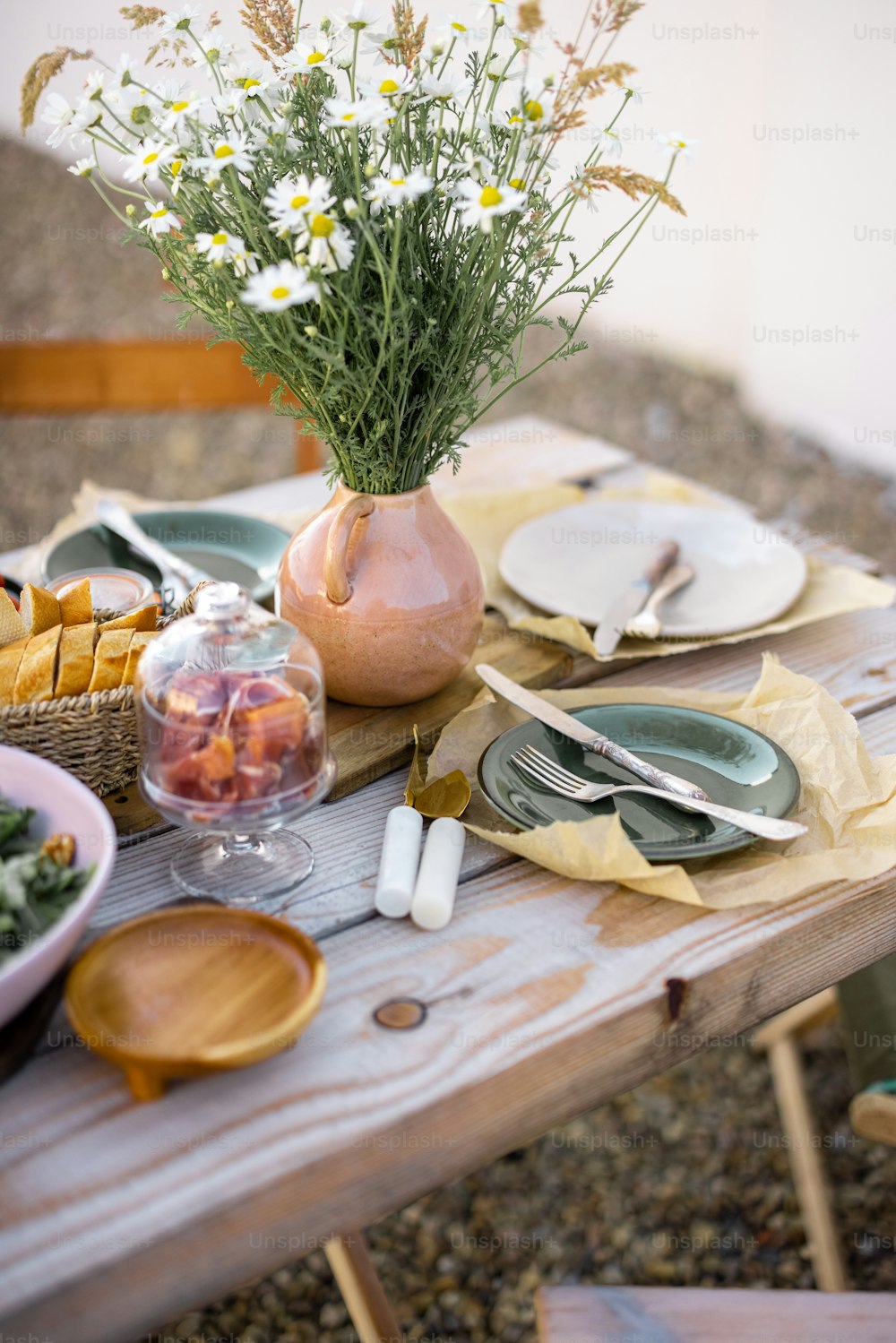Beautifully served wooden table in natural boho style outdoors. Dining table decorated with field flowers, dishes and fresh food