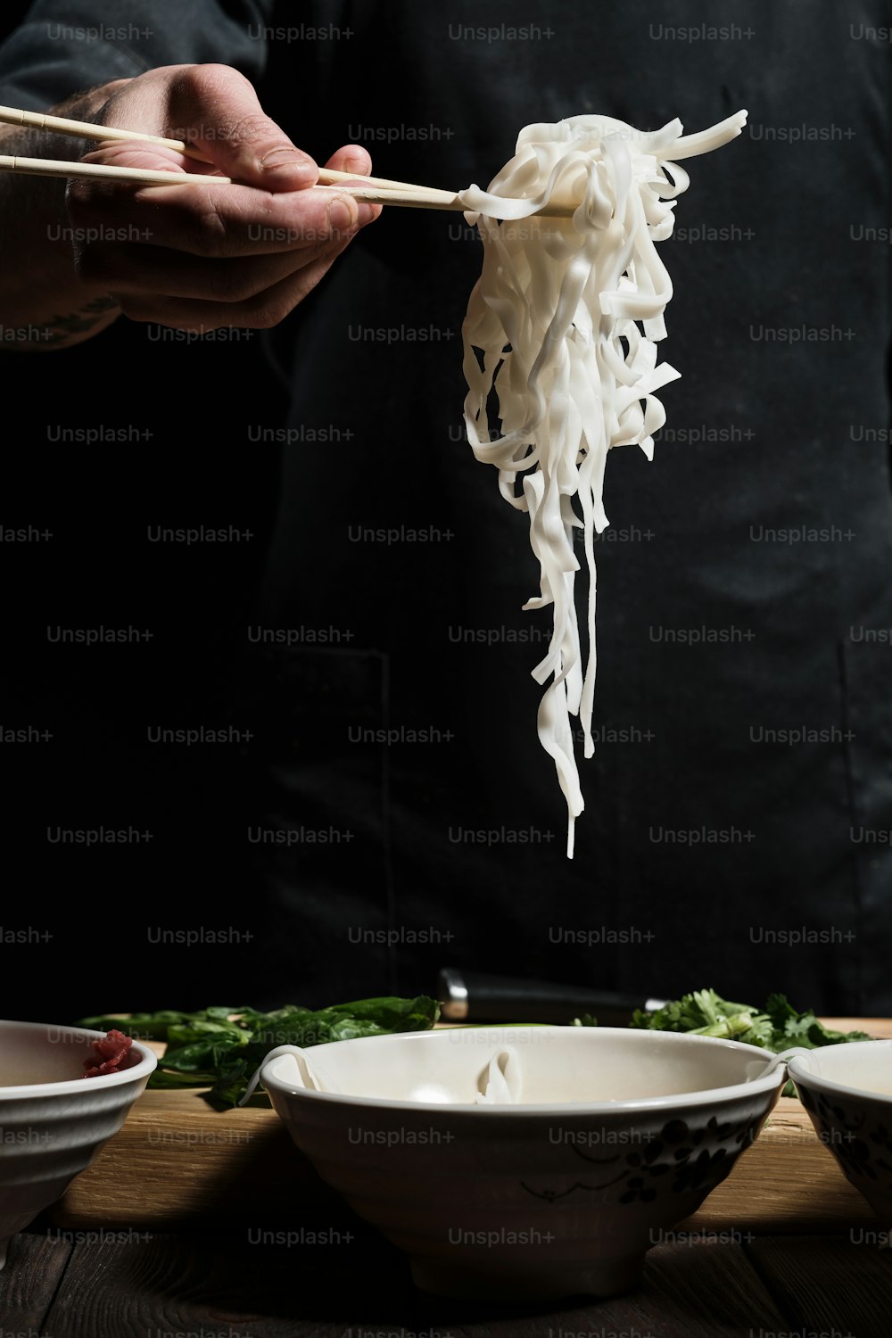 Primo piano delle mani dello chef che raccolgono i noodles dalla ciotola