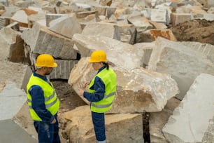 Two contemporary builders in workwear interacting between huge blocks at quarry