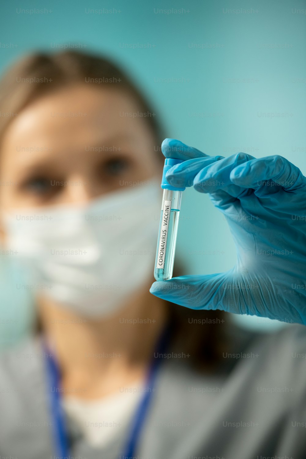 Primer plano de una enfermera con guante azul sosteniendo un tubo de ensayo de la vacuna contra el coronavirus mientras se prepara para la vacunación