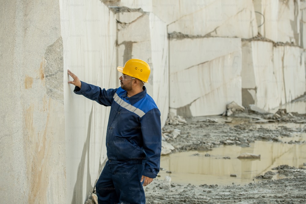 Junger Baumeister in Arbeitskleidung berührt weiße Blockwand rund um den Steinbruch