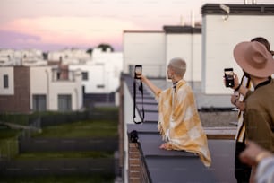 Young people enjoy beautiful urban view from the rooftop terrace at dusk. Friends hang out on the roof party at evening