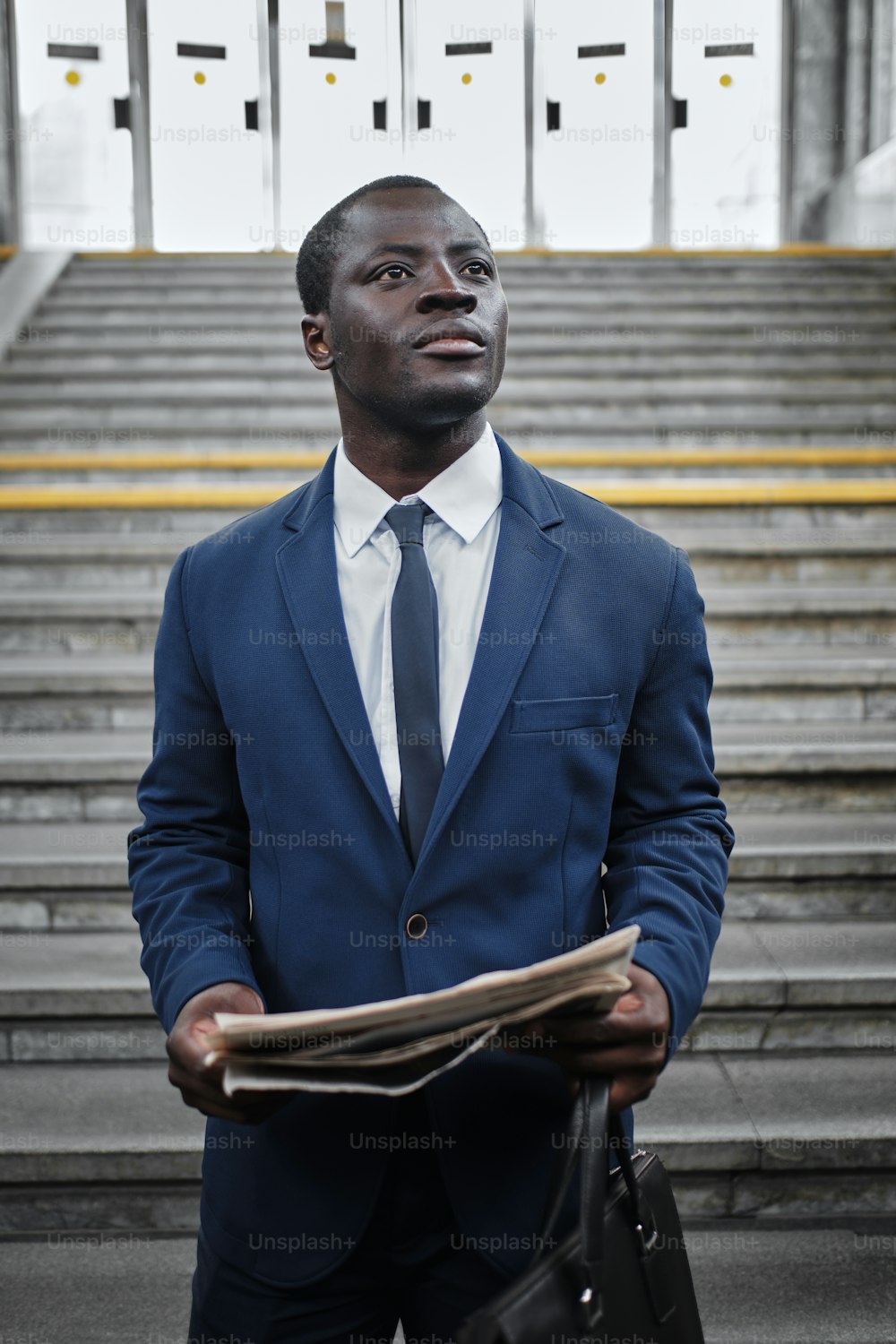 Retrato de un hombre negro serio y seguro de sí mismo vestido con traje azul y corbata, leyendo un periódico en la estación de metro