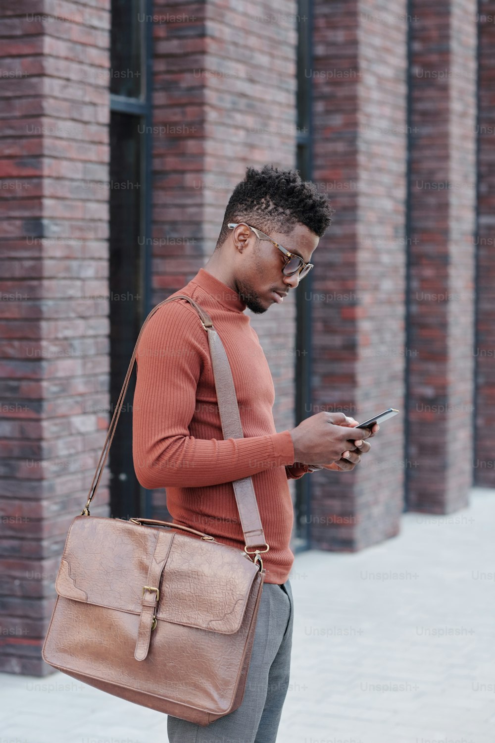 Uomo d'affari africano con la borsetta sulla spalla che scorre nello smartphone