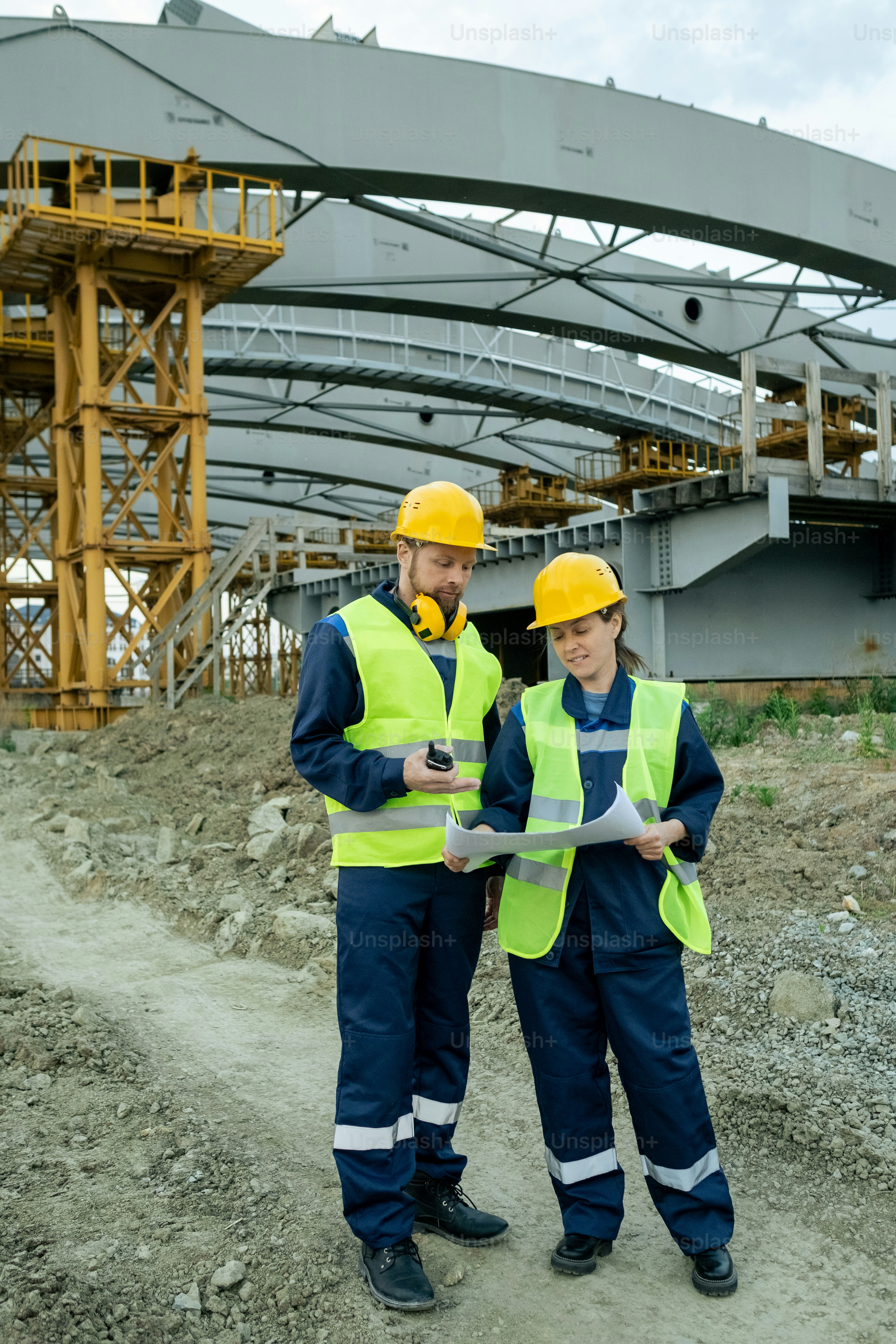 Two builders in uniform looking at sketch on blueprint while discussing it