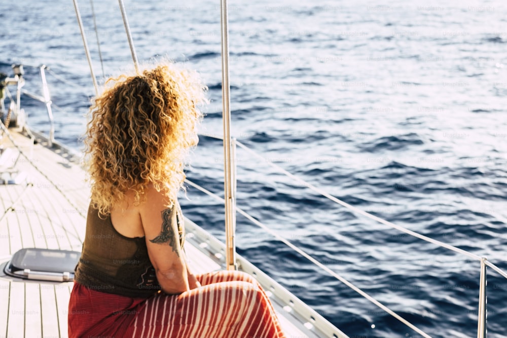 Back view of blonde curly long hair woman with tattoo enjoying the trip on a boat - concept of lifestyle in summer holiday vacation for tourist people