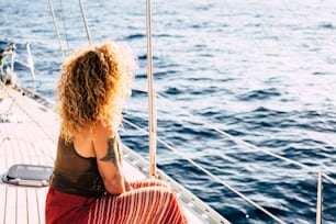 Back view of blonde curly long hair woman with tattoo enjoying the trip on a boat - concept of lifestyle in summer holiday vacation for tourist people