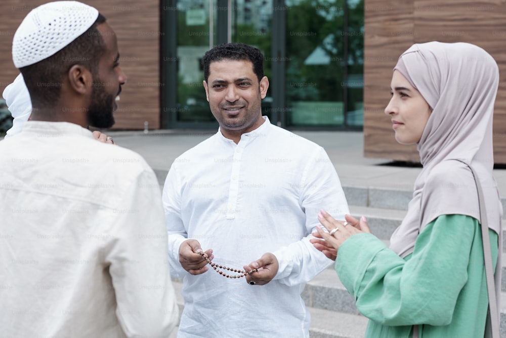 Grupo de conteúdo ambicioso jovens empresários islâmicos em pé em círculo ao ar livre e discutindo o desenvolvimento de negócios