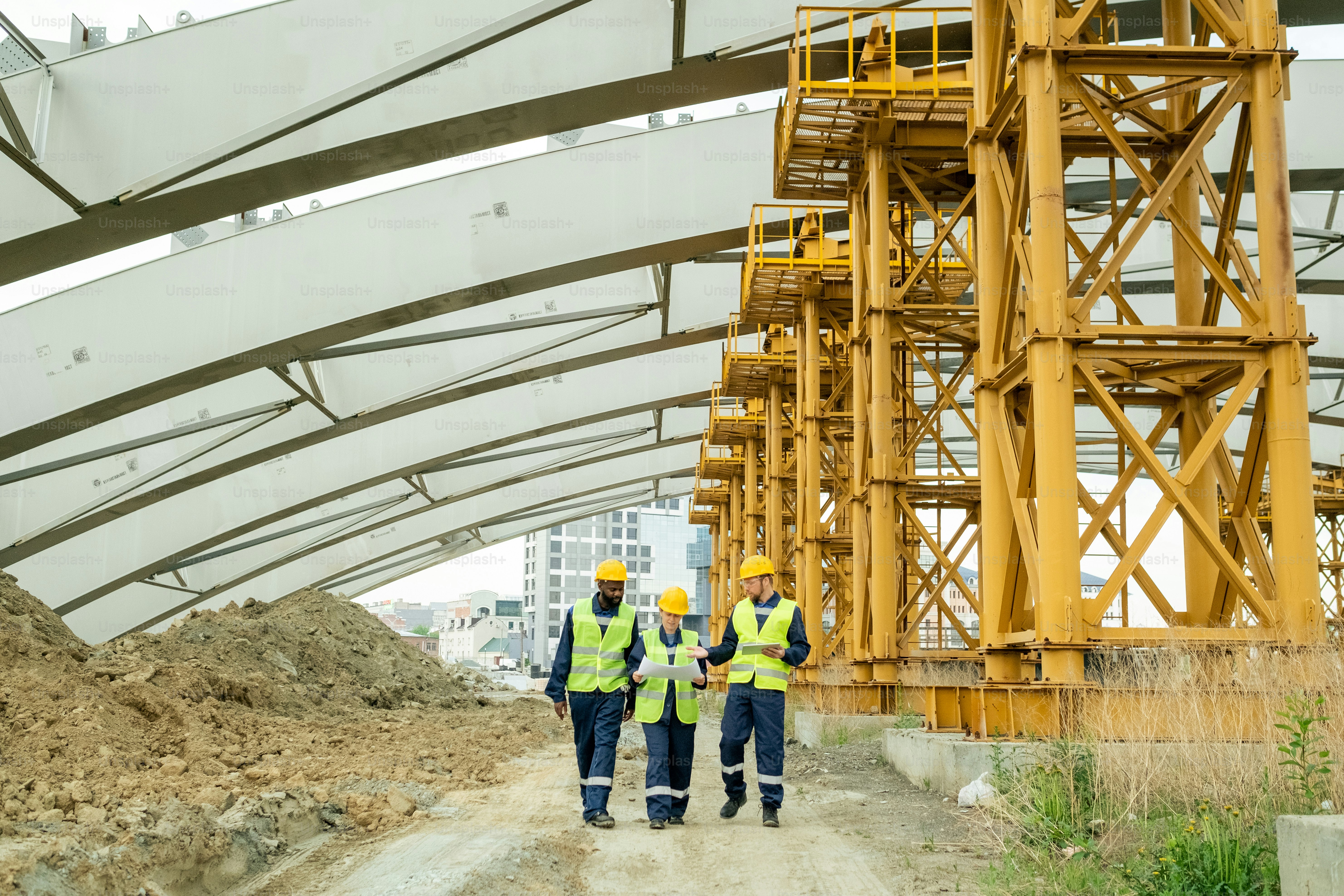 Group of engineers examining blueprint and using digital tablet while working through the construction site, they controlling the construction