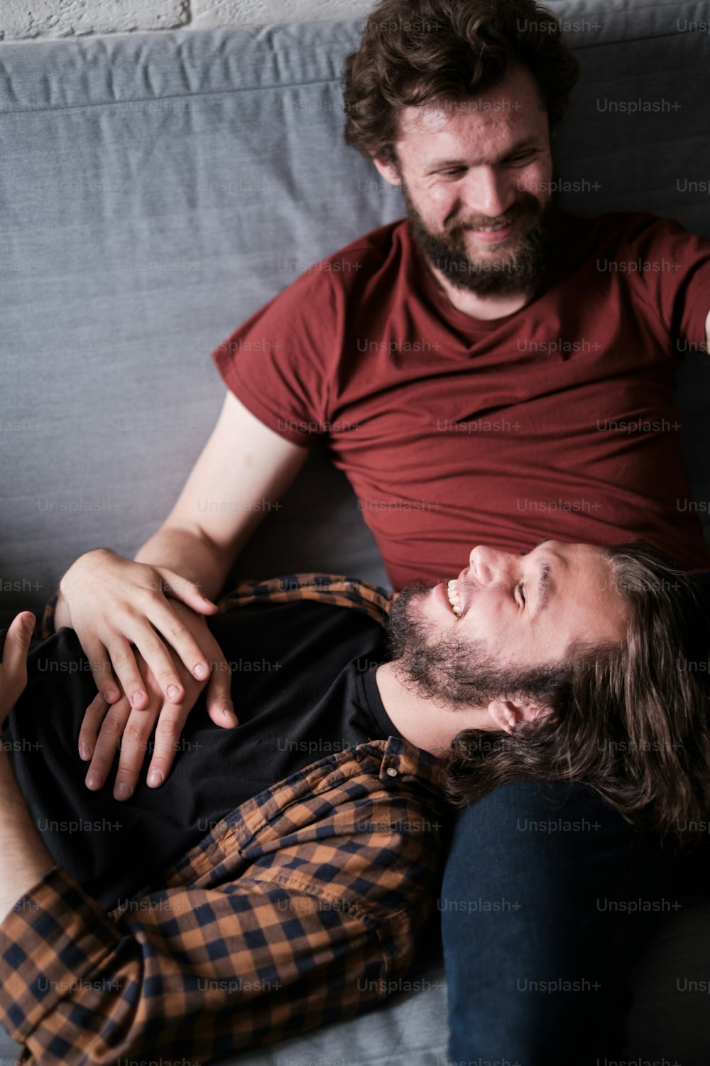 Porträt von zwei mittelalten bärtigen Männern, die auf dem Sofa liegen, entspannen, Zeit miteinander verbringen