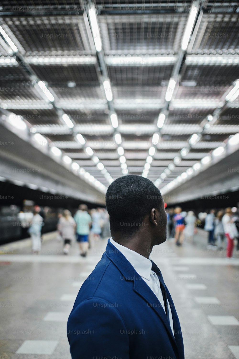 Vertical portrait of african businessman in blue suit and tie turned around while walking at underground subway station