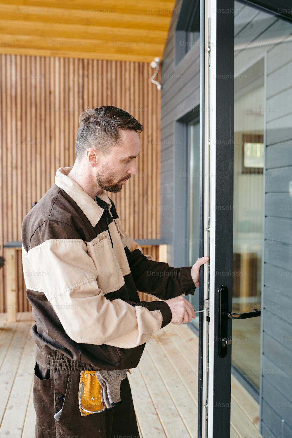 Young repairman fixing lock in large transparent door of house