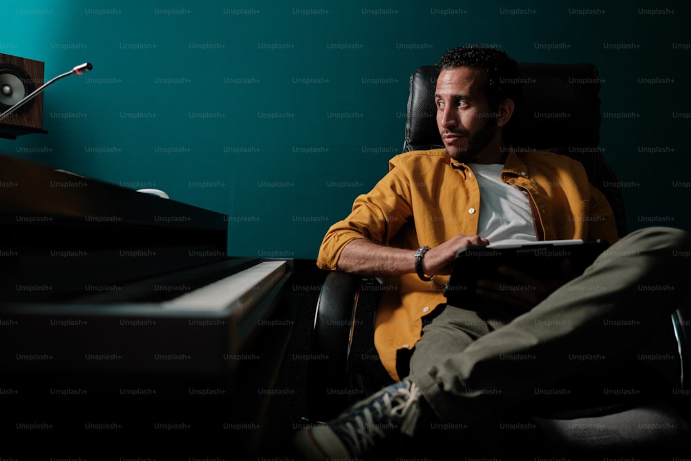 Retrato do homem marroquino na camisa amarela usando o tablet e o controlador do mixer do palco no estúdio de gravação profissional