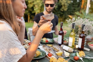 Young friends drinking alcohol having a lunch with vegetables and fish outdoors