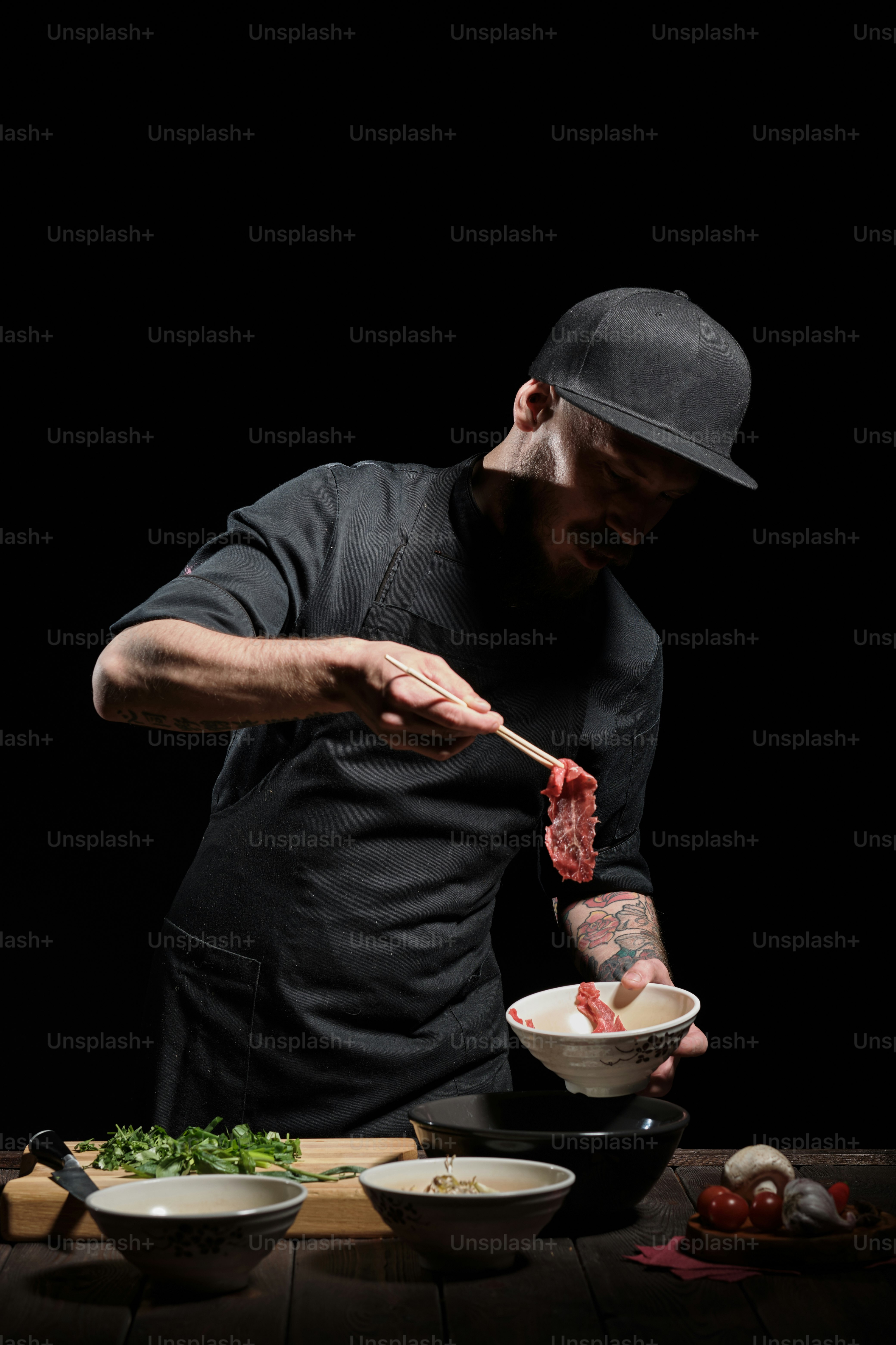 Portrait of male chef adding meat with chopsticks to the noodle bowl