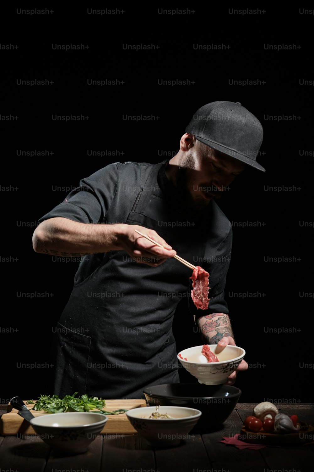 Ritratto di chef maschio che aggiunge carne con bacchette alla ciotola di noodle