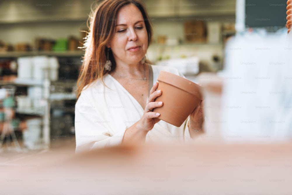 Brunette middle aged woman in white dress buys clay flower pots at hardware store, selective focus
