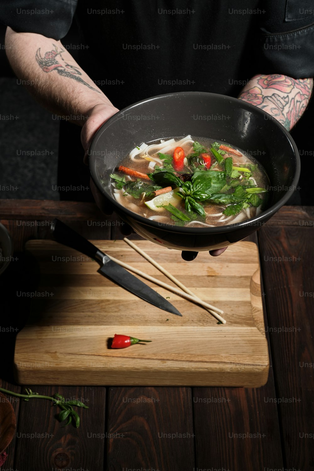 Nahaufnahme der Hände des Küchenchefs, die das Gericht mit frisch zubereiteten asiatischen Speisen halten und es in Richtung Kamera anbieten