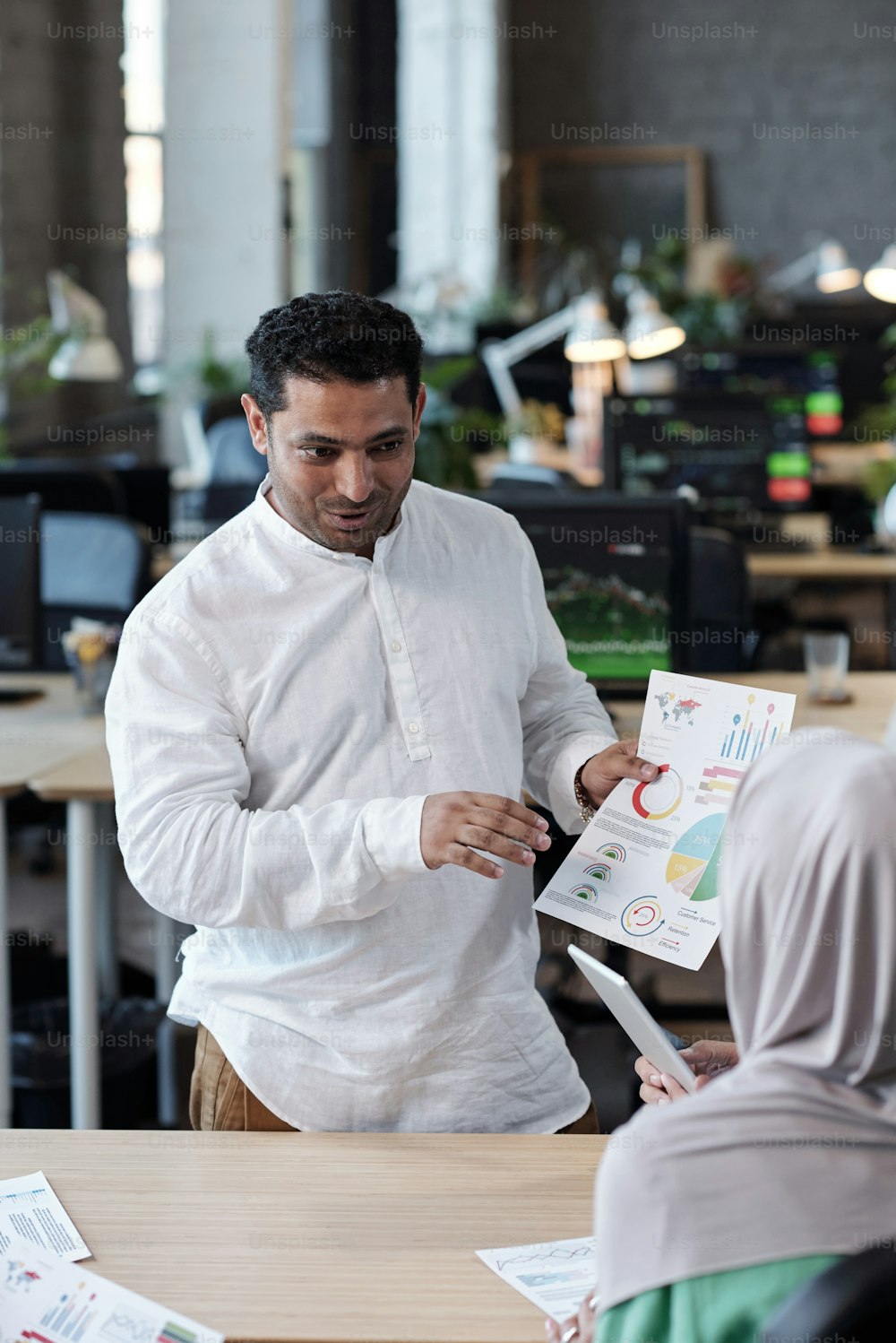 Contemporary businessman with financial document looking at female colleague in hijab during discussion