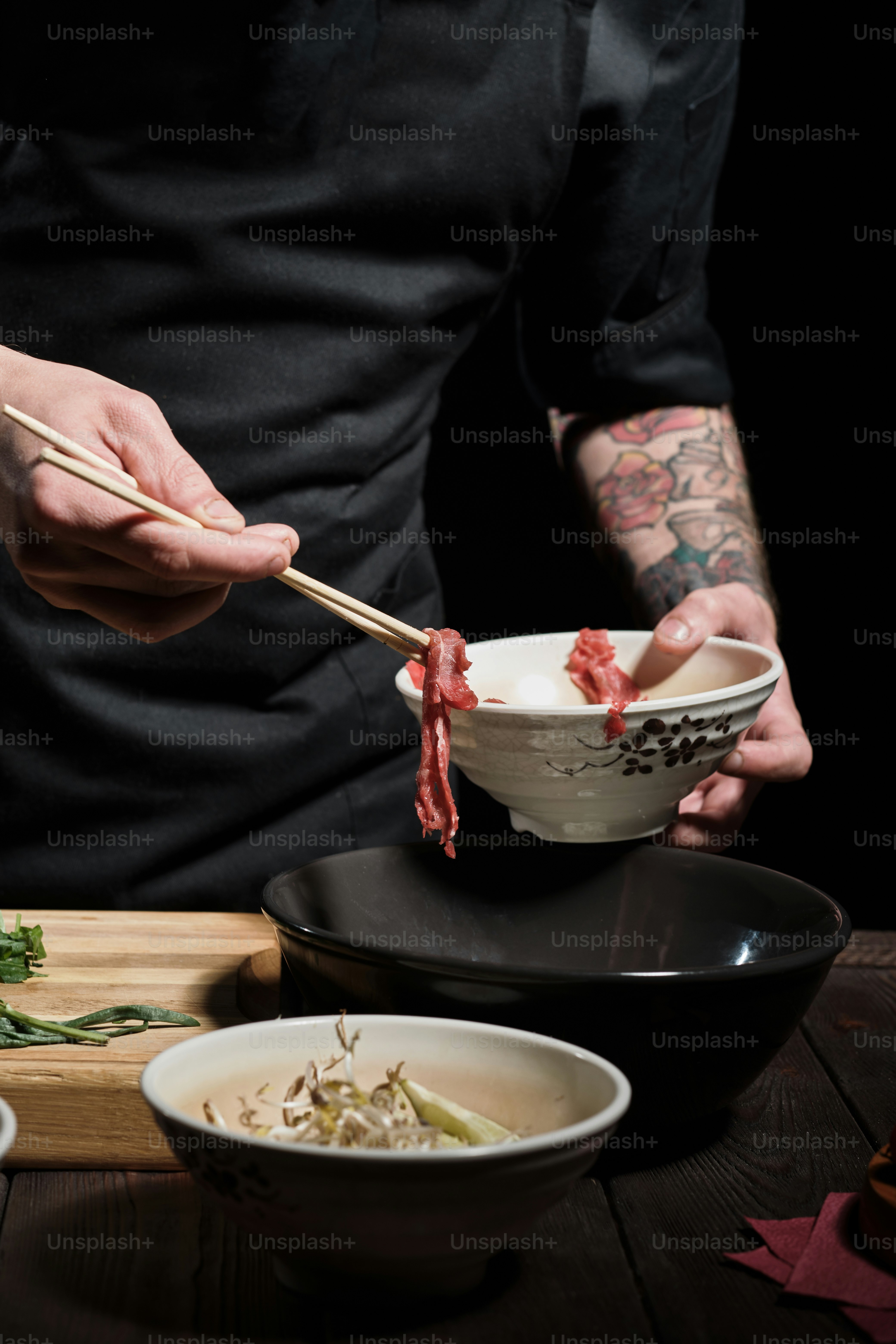 Close up of chef's hands adding beef to noodle bolw with chopsticks
