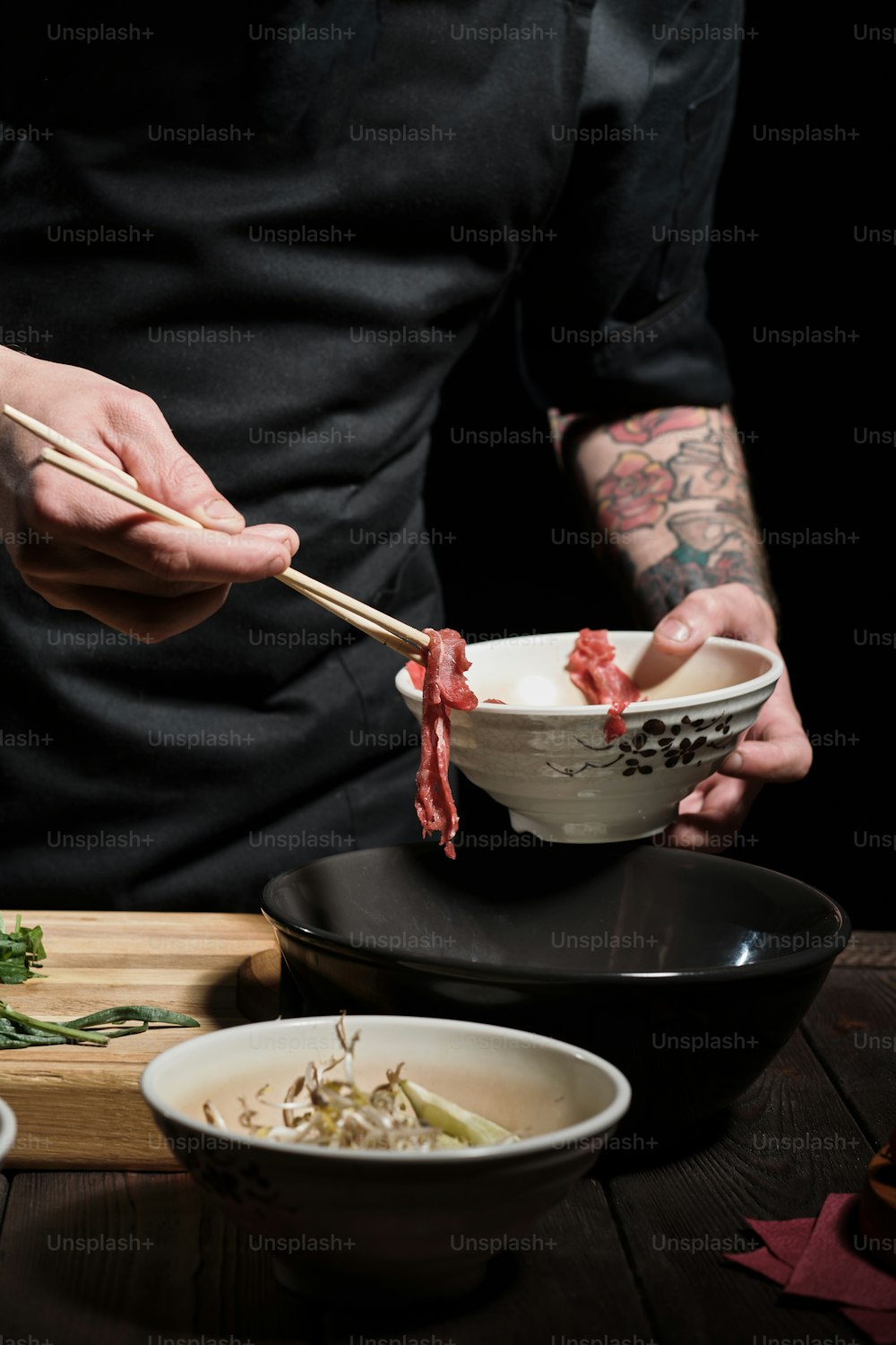 Primo piano delle mani dello chef che aggiungono carne di manzo a noodle bolw con bacchette
