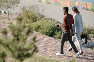 Zwei junge interkulturelle Kollegen diskutieren über Arbeitsmomente, während sie sich im öffentlichen Park entlang der Straße bewegen