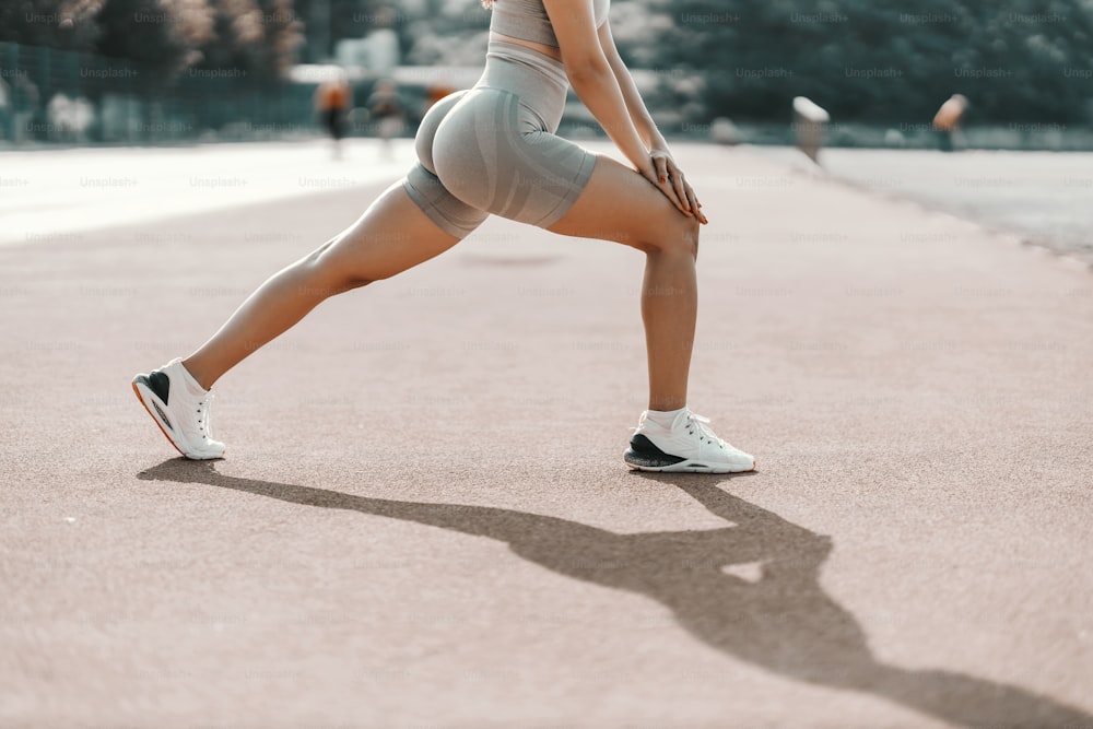 前に出て、トレーニングで脚の筋肉を伸ばす。タイトなグレーのフィットネスウェアを着た女性が、エクササイズ中に脚の筋肉を伸ばしています。トレーニング中の女性のハンサムな体の側面ショット