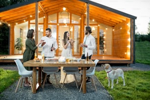 Friends having a dinner with pizza on the backyard of the modern house decorated with lights during the evening time outdoors