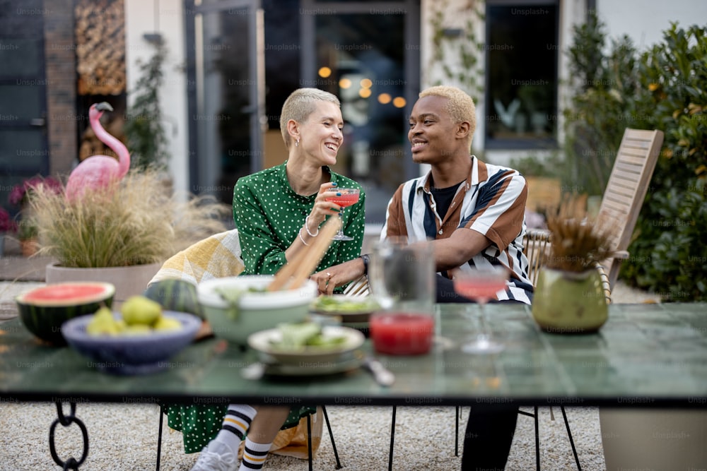 Multiracial couple having dinner at backyard of their country house. Idea of healthy eating and modern lifestyle. Black man and european woman having heart-to-heart conversation enjoying time together