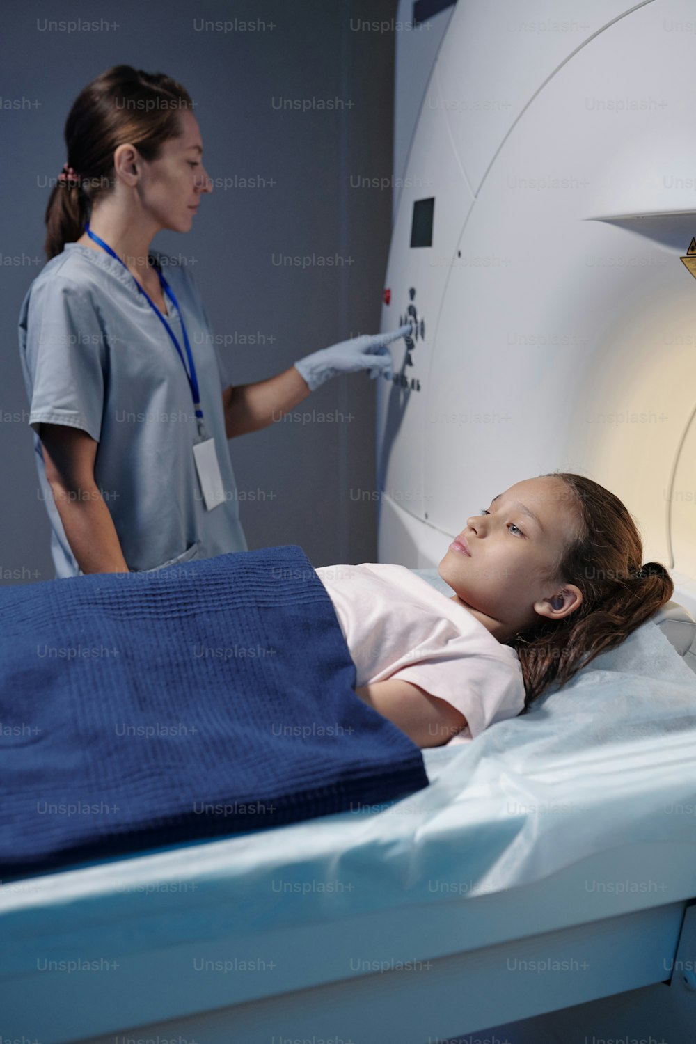 MRIスキャン検査を受けている小さな患者の間にコントロールパネルのボタンを押す女性医師