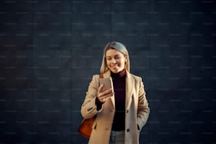 A woman in coat standing outdoors and smiling at the phone.
