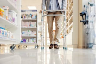 薬局で歩行器のサポートを受けて歩く年配の男性。