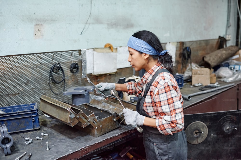 Young female worker of industrial plant choosing huge wrench for repair work while standing by workbench with metallic toolbox