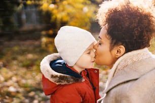 Caregiver kissing kindergarten's boy nose outdoors. Caring caregiver kissing kindergarten child on the nose outdoors.