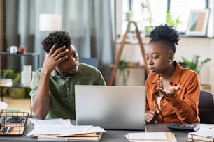 Young African woman and man looking at laptop screen while female explaining online data to male colleague