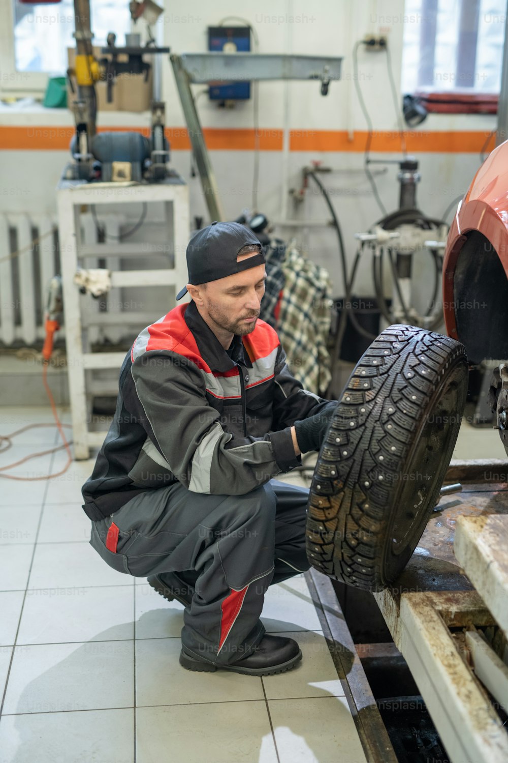 Vertical full length portrait of male mechanic changing tires on car while working in auto repair shop