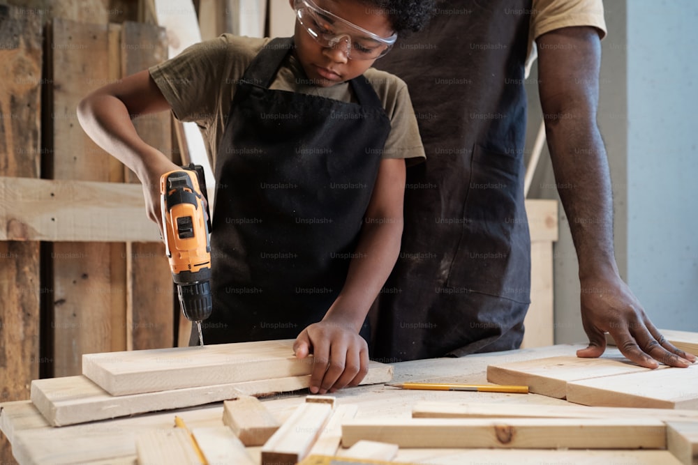 Retrato recortado de un lindo niño afroamericano construyendo una casa para pájaros en un taller con papá