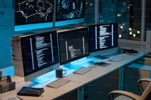 Posto di lavoro di ingegneri informatici contemporanei con tre computer in piedi sulla scrivania in un grande ufficio openspace