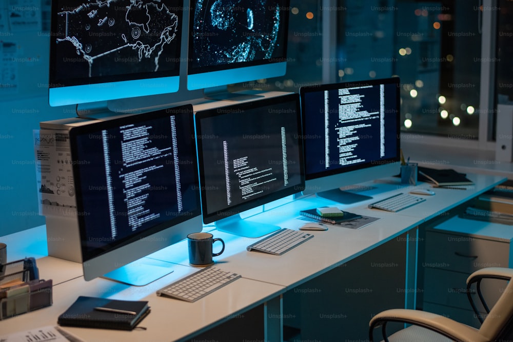 Workplace of contemporary it-engineers with three computers standing on desk in large openspace office