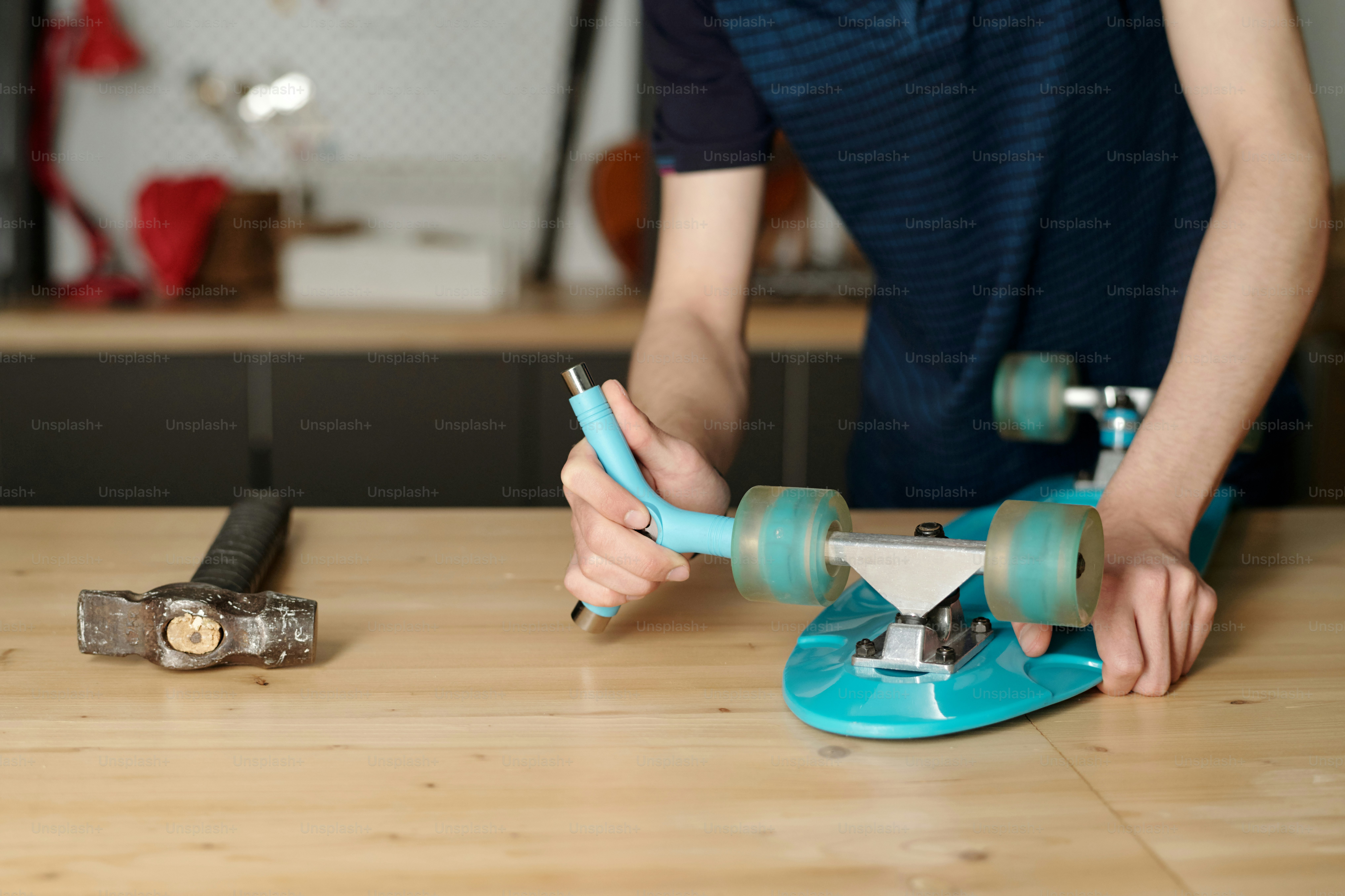 Contemporary adolescent boy with blue wrench fixing wheels of skateboard while bending over workbench with hammer
