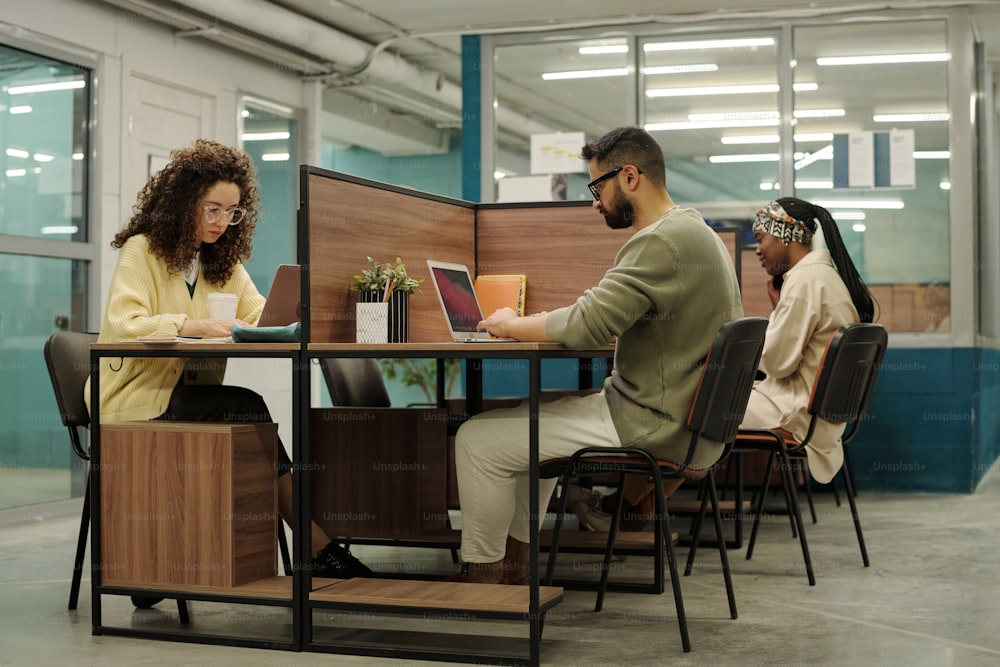 オープンスペースのオフィスで職場のそばに座り、オンライン情報を分析する若い異文化間の同僚のグループ