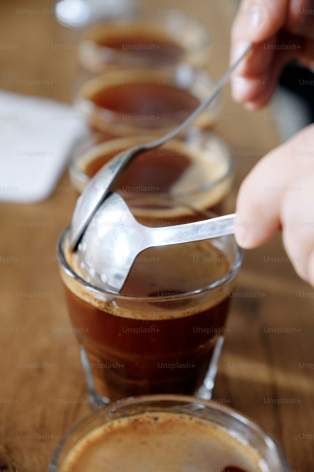 Close up of man's hands tasting freshly brewed coffee in glass cup, using spoon, examining coffee taste and flavour at coffee cupping test for barosta