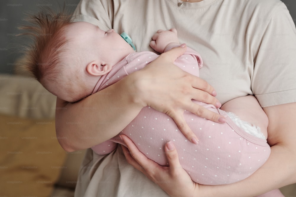 おしゃぶりを口にくわえた愛らしい小さな赤ちゃんが母親の手で安らかに眠っている