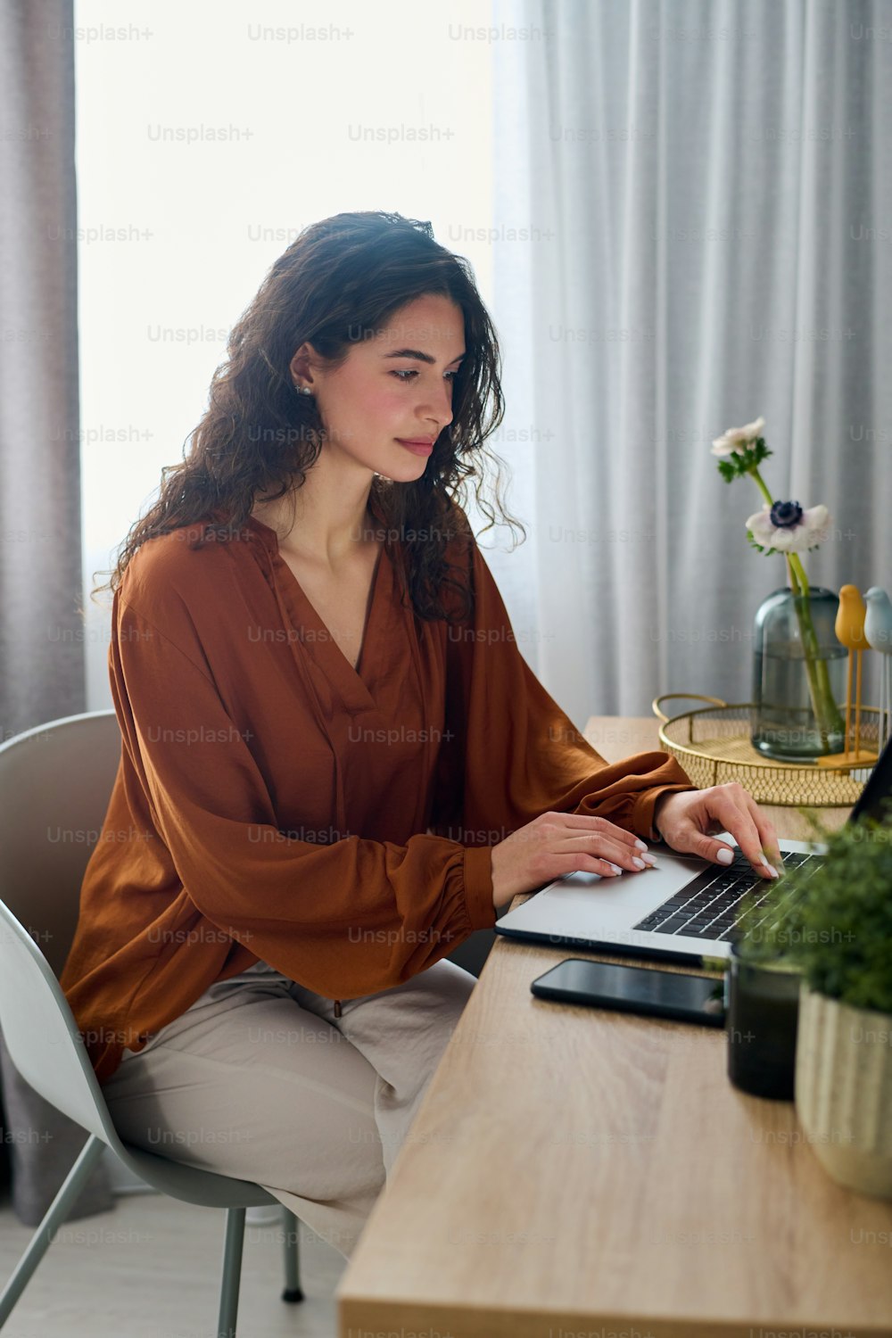 Jeune femme d’affaires brune en tenue décontractée assise devant un ordinateur portable près d’un bureau tout en travaillant sur un nouveau projet à partir d’un bureau à domicile