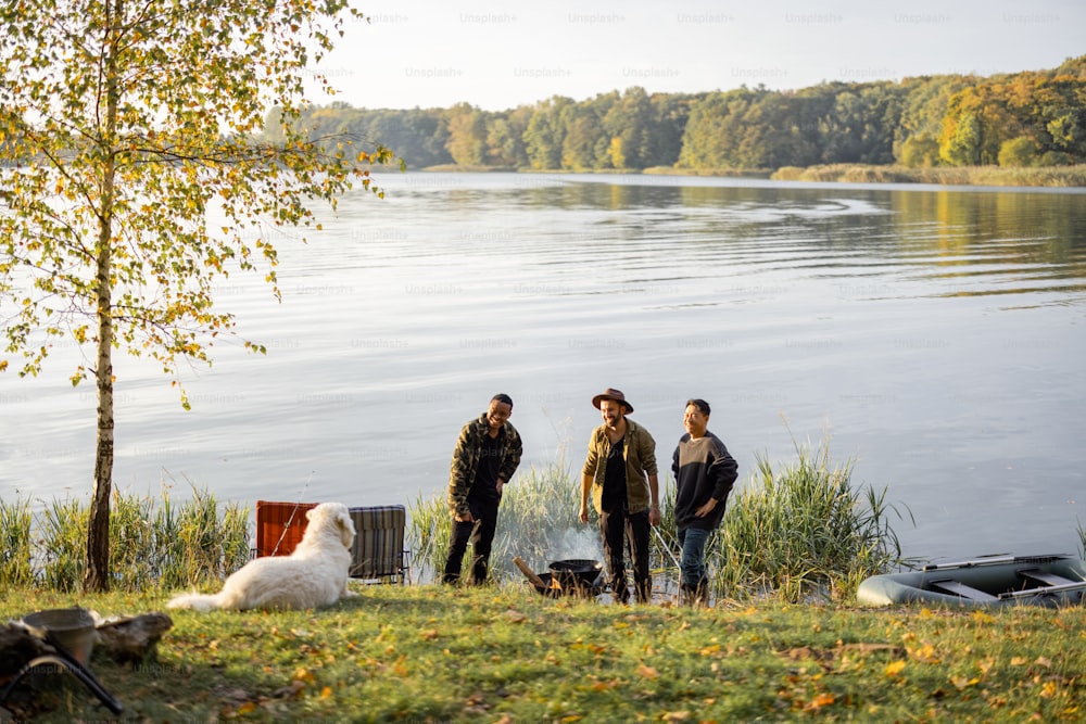 Paesaggio di un bellissimo lago con un gruppo di amici maschi che fanno un picnic mentre pescano sulla costa. Tempo libero, weekend e vacanze nella natura