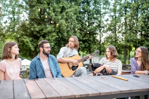 Jóvenes amigos divirtiéndose juntos tocando la guitarra sentados en la mesa al aire libre en el parque