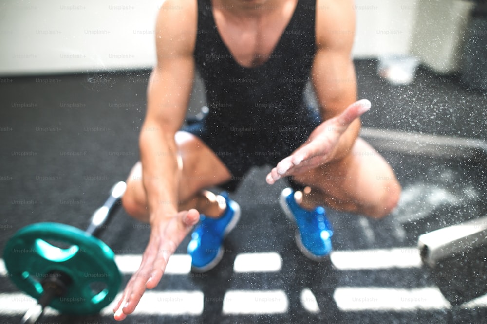 Nicht erkennbar fitter junger Mann im Fitnessstudio mit Langhanteln, die seine Hände mit Magnesium beschmieren.