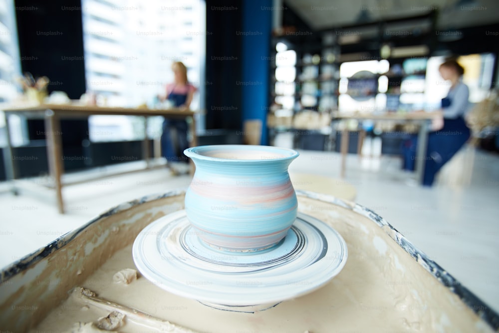 New creative clay jug with painted blue stripes rotating on pottery wheel in workshop