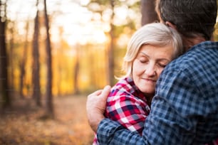 Active senior couple on a walk in a beautiful autumn forest. Unrecognizable man and woman hugging, eyes closed.